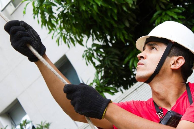 Técnico de içamento com capacete e luvas guiando a corda